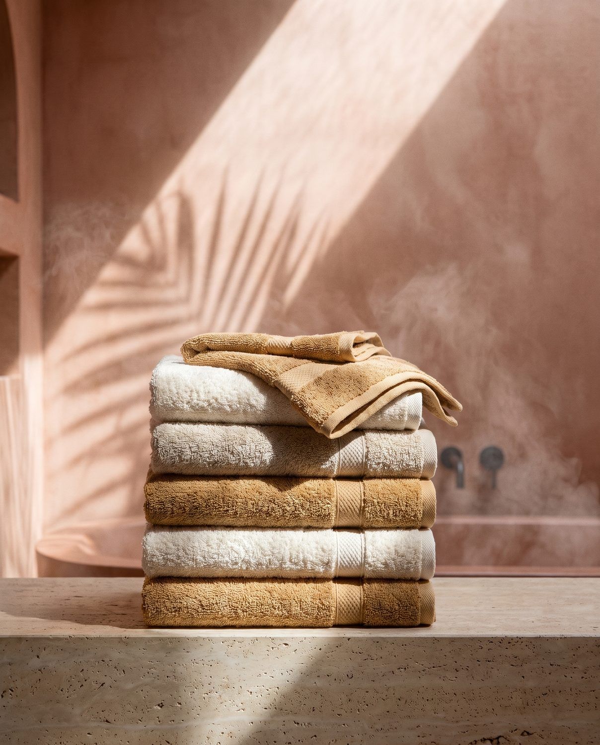 A stack of towels in the bathroom, palm shadow on the plaster